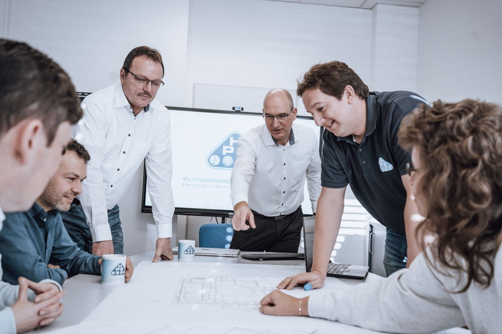Das Projektteam von HPS Hain betrachtet gemeinsam einen Planentwurf, der auf dem Tisch liegt.